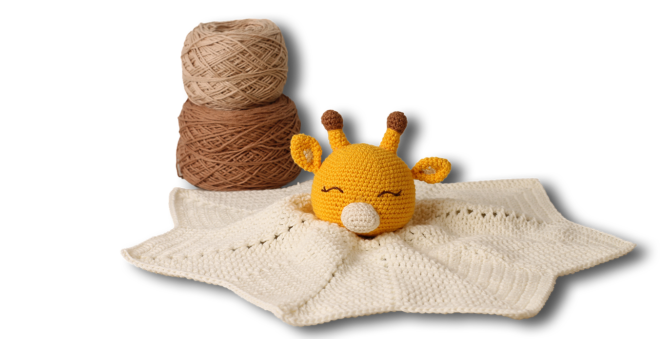 Jirafita amigurumi sobre mantita de apego junto a ovillos y aguja de crochet